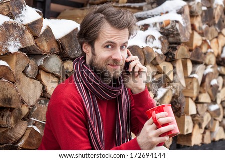 Close up portrait of happy smiling forty years old caucasian man talking on a mobile phone and drinking hot tea outdoor countryside during winter
