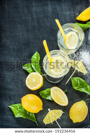 Lemonade with lemons and fresh wet leaves on black chalkboard from above. Background layout with free text space.