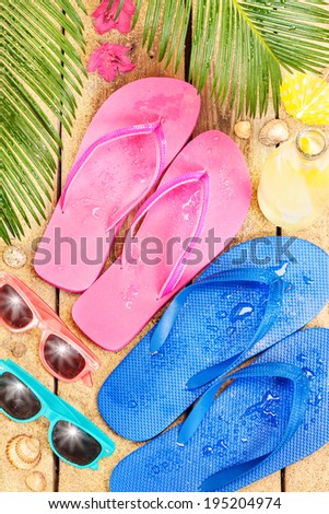 Summer holiday (vacation) tropical beach from above - palm tree leaves, exotic flowers, sunglasses and flip flops on sand.