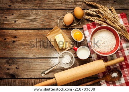 Baking cake in rural kitchen - dough recipe ingredients (eggs, flour, milk, butter, sugar) on vintage wooden table from above. Background layout with free text space.