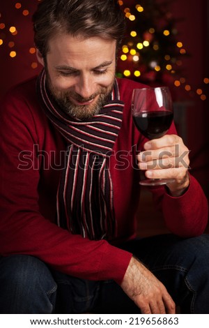 Christmas party concept - happy smiling forty years old caucasian man drinking wine. Dark red with lights as background.
