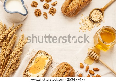 Rural or country breakfast - bread rolls, honey jar, milk, nuts, wheat on white wood from above. Background layout with free text space.