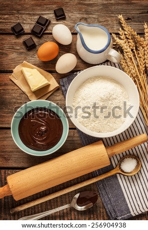 Baking chocolate cake in rural or rustic kitchen. Dough recipe ingredients (eggs, flour, milk, butter, sugar) on vintage wood table from above.
