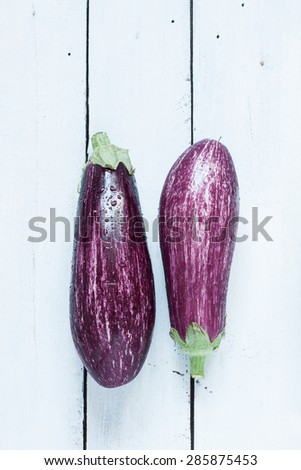 Purple eggplant (aubergine) on white planked wood table from above. Fresh harvest from the garden. Background layout with free text space.
