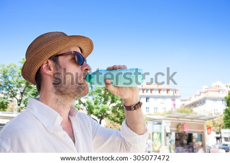 Forty years old caucasian tourist man drinking water out of bottle outdoor in a hot city. Summer holiday traveling.