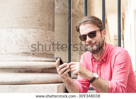 Happy smiling forty years old caucasian man in sunglasses touching mobile phone screen (smartphone) outdoor in the city.