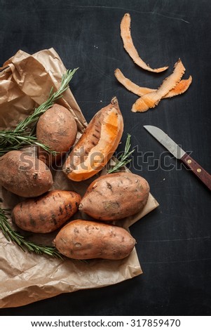 Peeling sweet potatoes with knife on black chalkboard background from above.