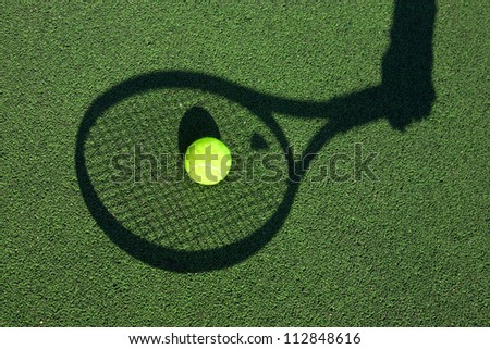 in action on a tennis court (conceptual image with a tennis ball lying on the court and the shadow of the player positioned in a way he seems to be playing it)