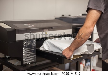 Professional graphic print technician work on digital t-shirt printing machine printer in printing production shop