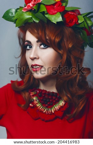 Beautiful sexy red-haired girl in a red dress with makeup and red lips with wreath  with flowers in her hair decoration of flowers around his neck smiling happy smile with teeth