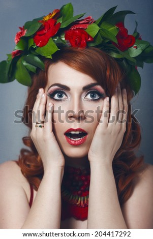 Beautiful sexy red-haired girl in a red dress with makeup and red lips with wreath  with flowers in her hair decoration of flowers around his neck smiling happy