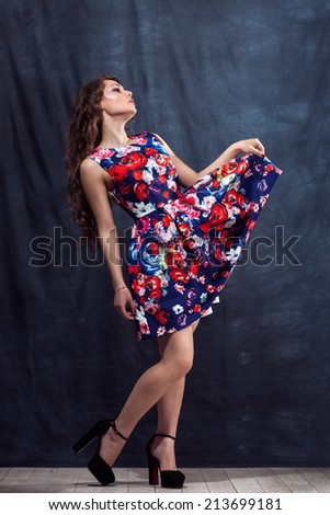young beautiful girl standing holding up dress up in colorful dress with makeup and long hair in natural black shoes in the studio