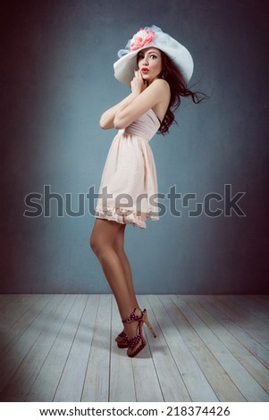 young beautiful sexy brunette girl with long flowing hair in a hat with makeup with a beautiful figure in a pink dress with long legs in shoes and heels pin up