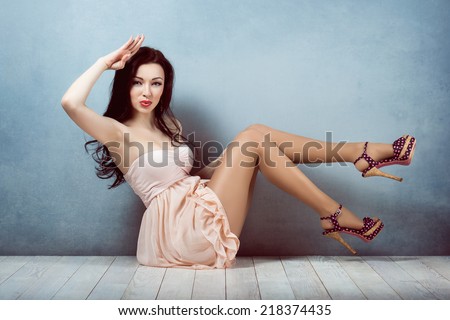Sexy young beautiful brunette with long hair, with a slender figure sitting on lifting legs up and salutes in a pink dress and make-up girl retro woman athletic and acrobatic pin up