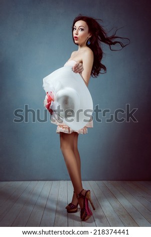 young beautiful sexy brunette girl with long flowing hair holding a hat with a make-up with a beautiful figure in a pink dress with long legs in shoes and heels pin up