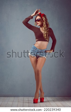 Beautiful young sexy blonde slim figure with a red armband with red lips in denim shorts in red high heels with long legs wearing glasses Pin Up