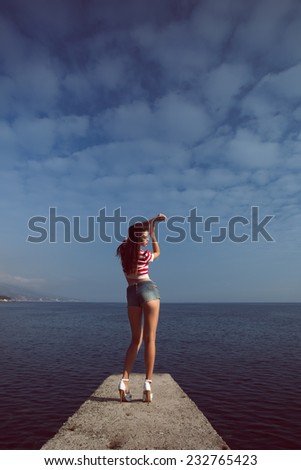 pin up young beautiful girl on the sea in short jeans and striped T-shirt with long hair  gulls water clouds wave dream figure with glasses emotions, smile with teeth, open mouth, red lipstick,