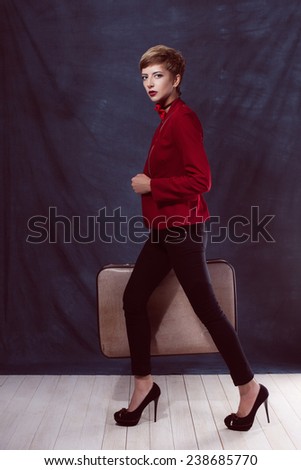 young sexy girl with a suitcase in a jacket and pants in bow tie with makeup movement is in a hurry