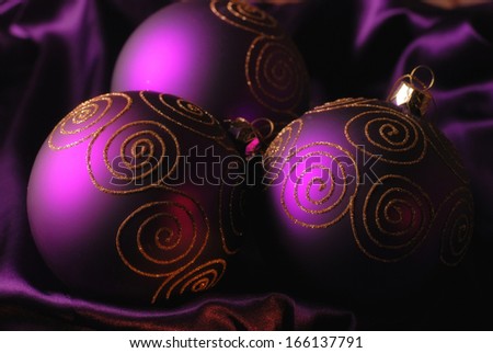 Three purple christmas balls with gold glitter on a shine silk background. Selective focus.