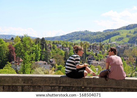 BERN, SWITZERLAND - MAY 8: Two young female students sitting on parapet with beautiful cityscape in Bern, Switzerland on May 08, 2013.