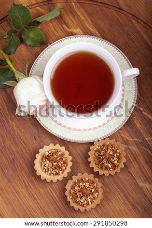 Cup of tea with cake and rose on wood table, view from above