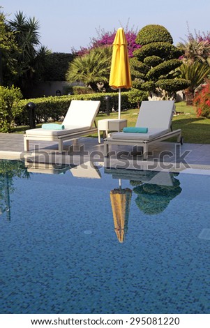 Vertical view with white outdoor furniture and yellow umbrella near the swimming pool for relax on summer resort. Selective focus