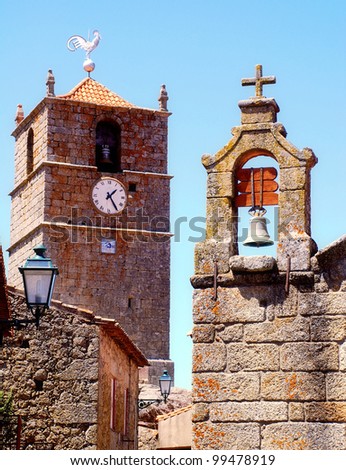 Old stone bell towers with clock, cross and weathercock on sky background (Portugal)
