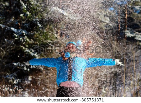red-haired girl in a blue jacket and blue hat with pom-poms enjoys the snowflakes in the winter woods