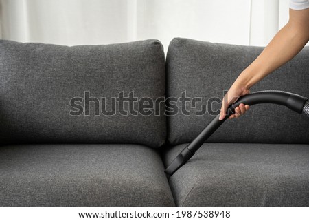Unrecognizable Asian man housekeeper using a vacuum machine vacuuming a dust on a sofa in living room close up. A man cleaning and sanitizing his house for hygiene living. Vacuum machine and housework