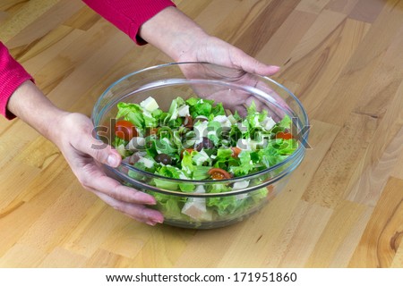 Women hands serving bowl of fresh vegetable salad with yellow cheese and chicken meet on a wooden table
