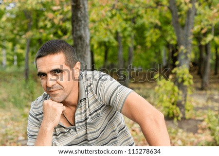 Attracive middle-aged thoughtful man sitting with his chin on his fist giving the camera a slight smile with a woodland backdrop and copyspace