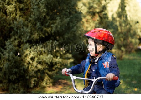 Little boy wearing a red crash helmet riding a bicycle outdoors on his own with copyspace