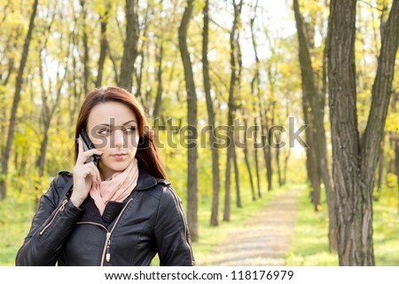 Beautiful trendy young woman waiting for a call to go through on her mobile phone as she stands on a path through woodland