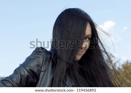 Woman with long brunette hair blowing in the breeze peering out with one eye from behind her tresses