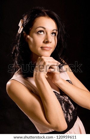 Pretty young woman standing staring up into space daydreaming or romanticising with a gentle smile on her face, studio portrait on a dark background