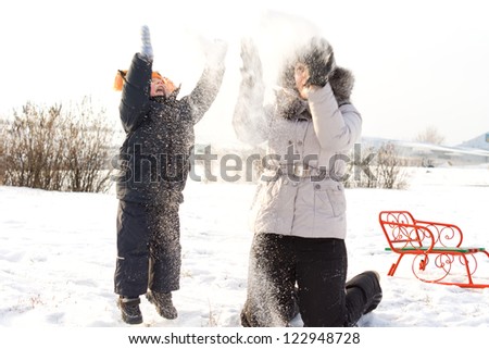 Young mother and small son having fun in the snow throwing it up in the air in a cold snowy winter landscape