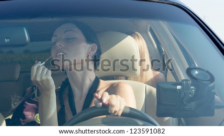 Woman driver applying lipstick using the rear view mirror in the car, view through windscren.