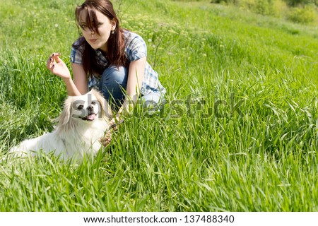 Young woman crouched down playing with her cute little dog in long green grass