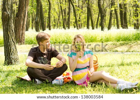 Photograph of a cute couple having food on picnic outside.