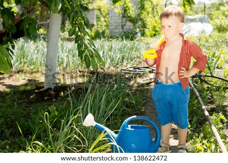 Youngster helping out in the veggie garden standing with a spade over his shoulder contemplating a blue plastic watering can