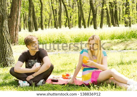 Attractive young couple enjoying a picnic sitting chatting on a rug on the grass amongst the trees