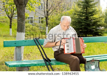 Handicapped senior man with one leg amputated above the knee sitting on a park bench playing the accordion