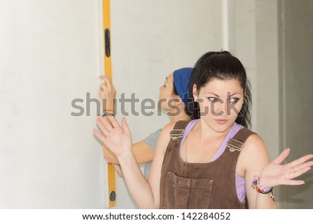 A woman talking something while the female carpenter working with spirit level at her back