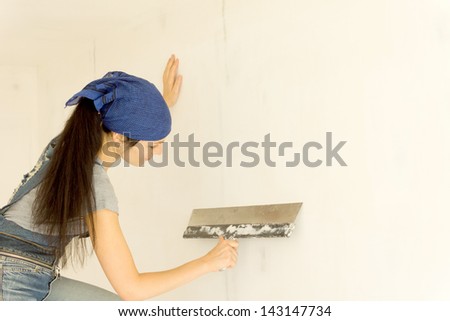 Female carpenter holds a paint scraper working on wall