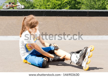 Young female teenage roller skater sitting on the tarmac rubbing her calf muscle to relieve a cramp or muscle strain sustained enjoying the sport