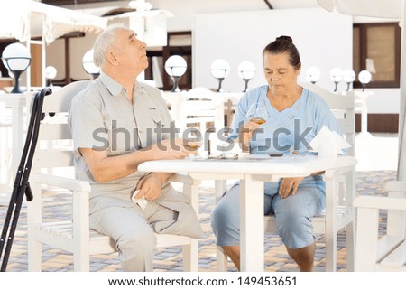 Elderly handicapped man on crutches and his wife sitting together at an outdoor restaurant enjoying a snifter of brandy