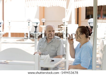Elderly couple enjoying drinks together sitting relaxing in the shade at an outdoor restaurant on a sunny summer day
