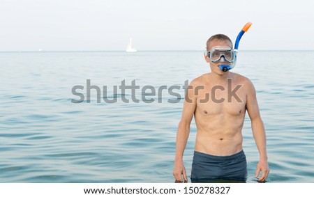 Young man wearing a snorkel and goggles standing in a calm sea as he prepares to go skindiving and exploring the marine underwater world