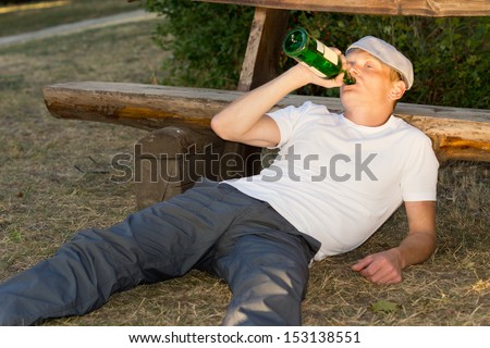 Alcoholic relaxing in a park lying on the ground with his bottle of liquor gulping down the contents