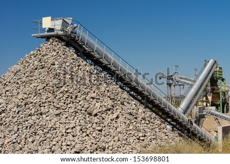 Open cast mining of stone for the construction industry with a mechanical conveyor belt emptying the processed crushed rock onto a pile or dump
